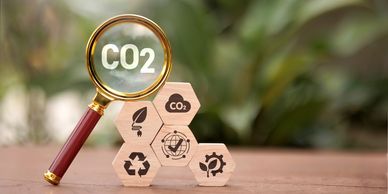 Magnifying glass highlighting CO2 text with eco-friendly icons on wooden blocks.