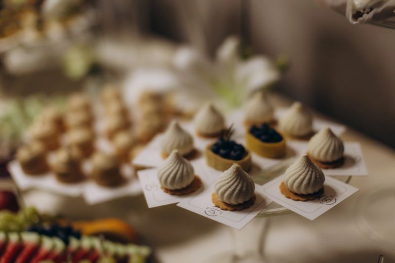 Elegant dessert buffet featuring a selection of white meringue pastries and blueberry tarts on individual pedestals, perfect for catering events