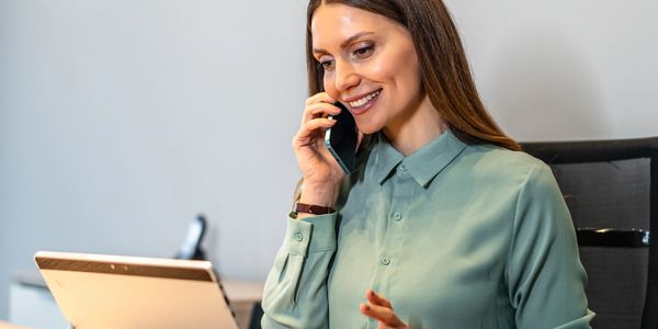 Woman in green shirt multitasking with phone and tablet at desk.