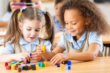 Two young girls playing with colorful building blocks at a table.