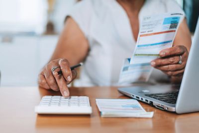 Person calculating bills with calculator and laptop.