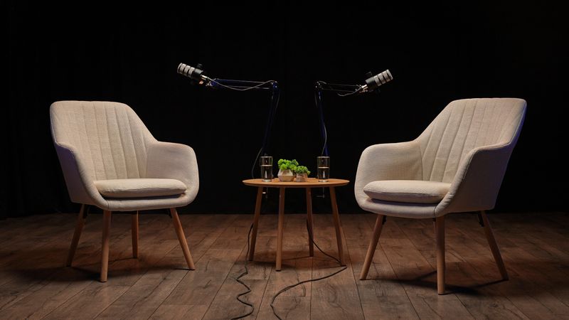Two stylish chairs face each other in a sleek podcast studio, ready for an enriching interview session. Microphones dangle from above, creating an inviting atmosphere for storytelling.