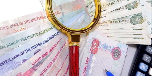Magnifying glass over UAE banknotes and calculator.