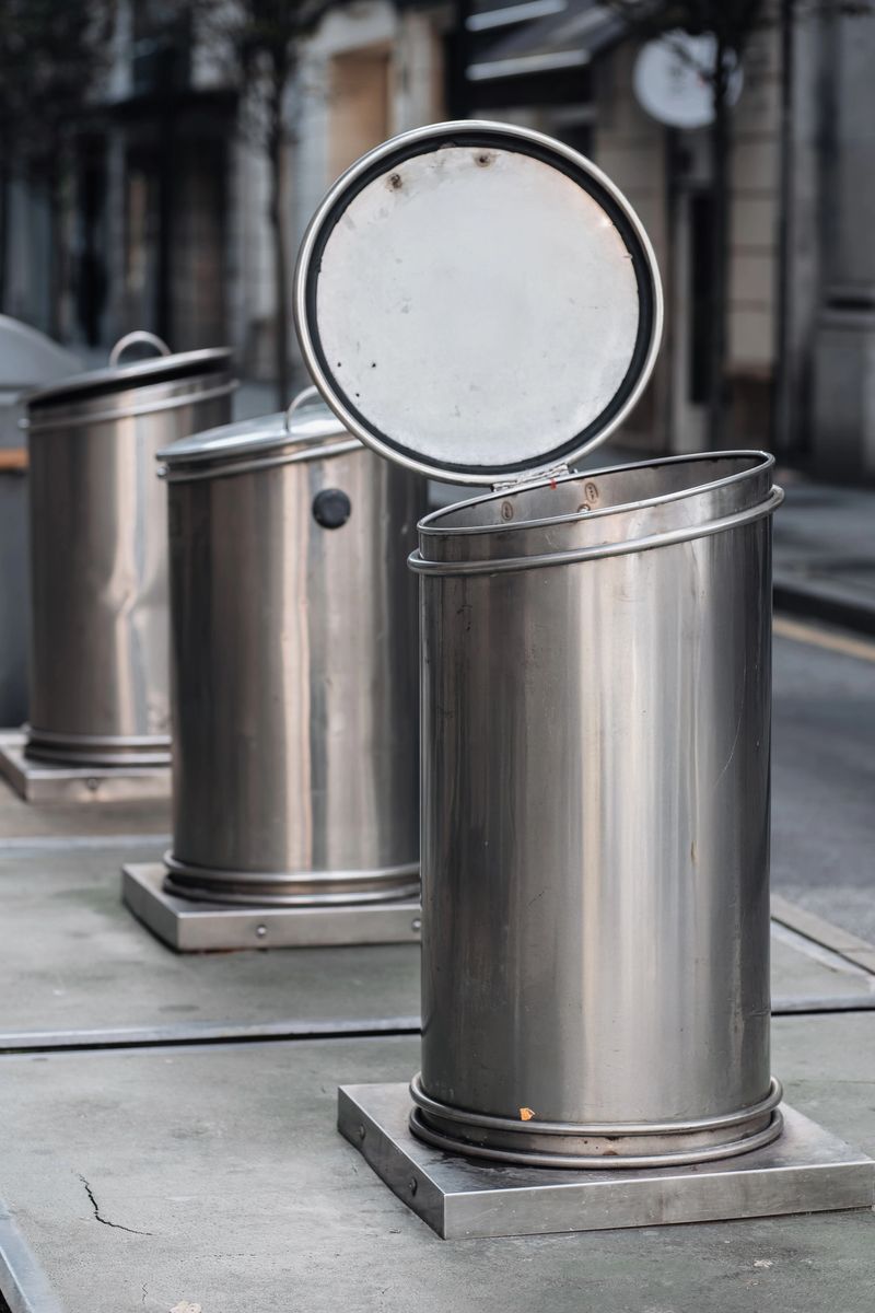 Modern stainless steel trash bins with open lids are positioned on a city street, showcasing urban waste management solutions and contemporary design aesthetics