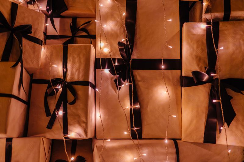 Gift boxes adorned with black ribbons are set against a backdrop of glowing fairy lights, enhancing the festive ambiance for holiday celebrations and special occasions