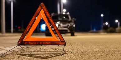 Orange emergency warning triangle on road with blurred car in background at night.