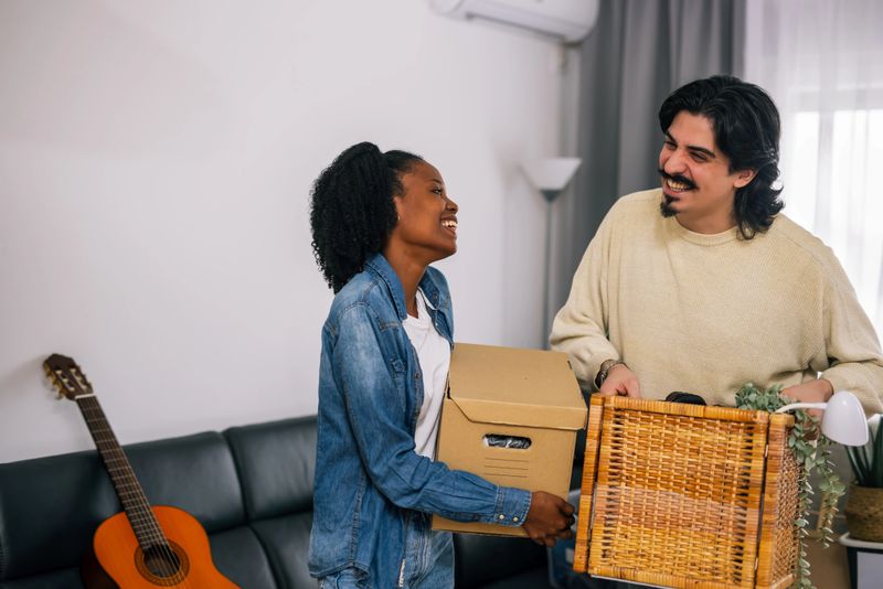 Multiracial couple carrying boxes together in their new apartment, organizing belongings and settling into their modern cozy home.