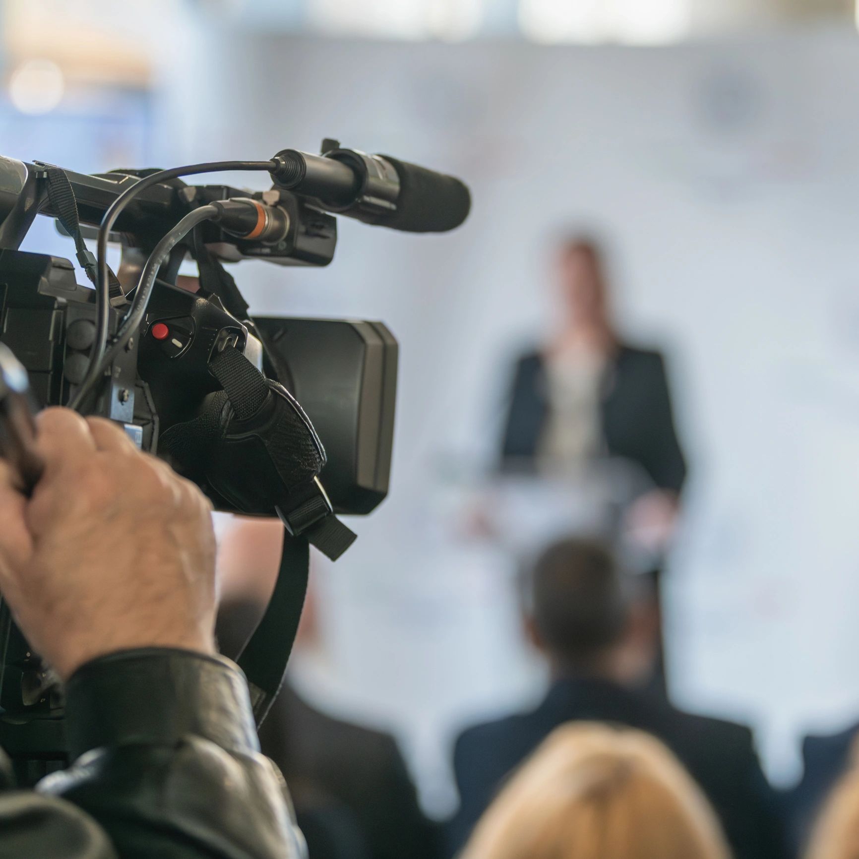 A professional video camera capturing a speaker at a conference or seminar.