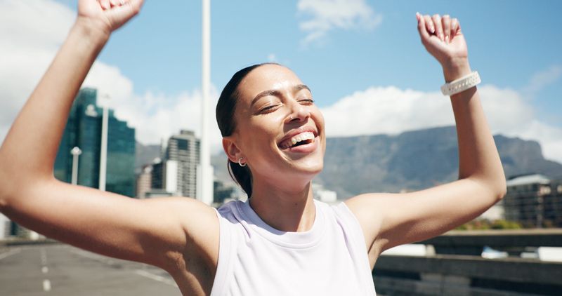 Happy woman, runner and winning with marathon success in city for fitness challenge or competition. Active, female person or winner with smile or fist pump for sport race, sprint or victory in town