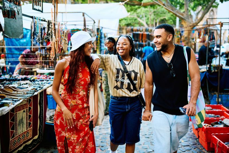 Vibrant friends walking side by side through a colourful market, smiling and talking together while enjoying movement, friendship, and relaxed urban travel.