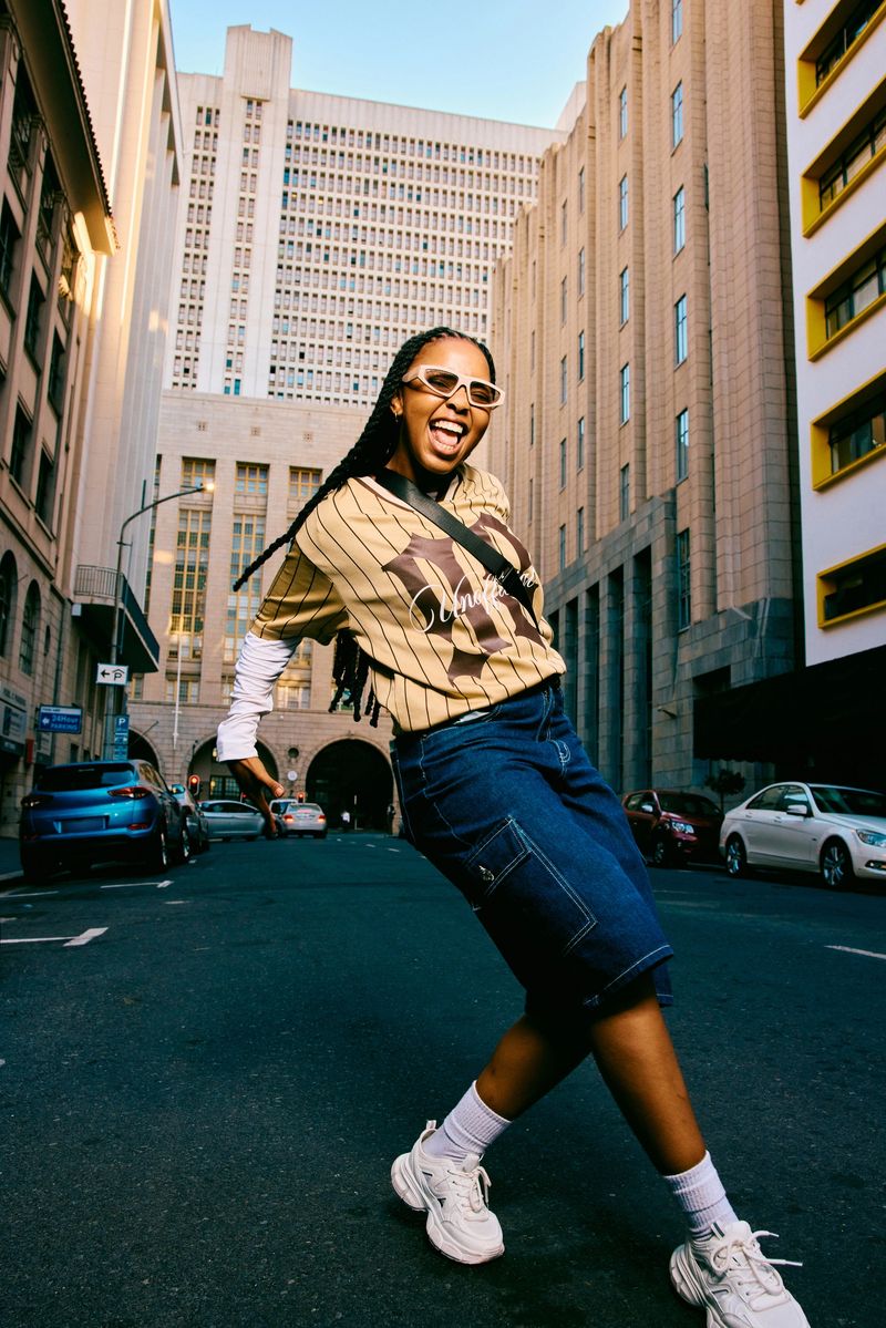 Side view of a confident young woman wearing casual streetwear dancing freely on a city street, expressing confidence, individuality, and playful youth culture energy.