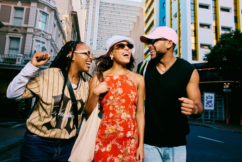 Group of fashionable young adults walking side by side on a city street, laughing and gesturing with energy, expressing friendship, confidence, and youthful urban lifestyle.