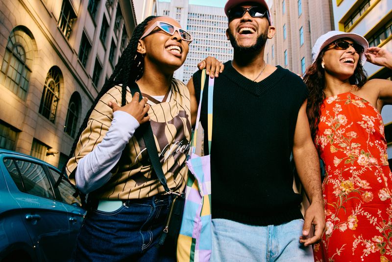 Low angle view of trendy friends walking closely together on a city street, smiling and chatting while showing relaxed attitude and youth travel vibes.