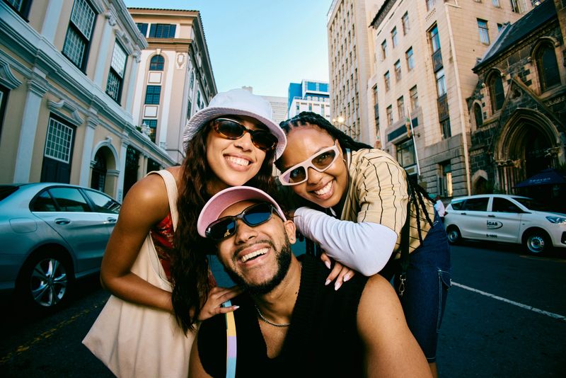 Closeup portrait of young adults in sunglasses and casual outfits smiling at the camera on a city street, capturing friendship, confidence, and modern urban travel lifestyle.