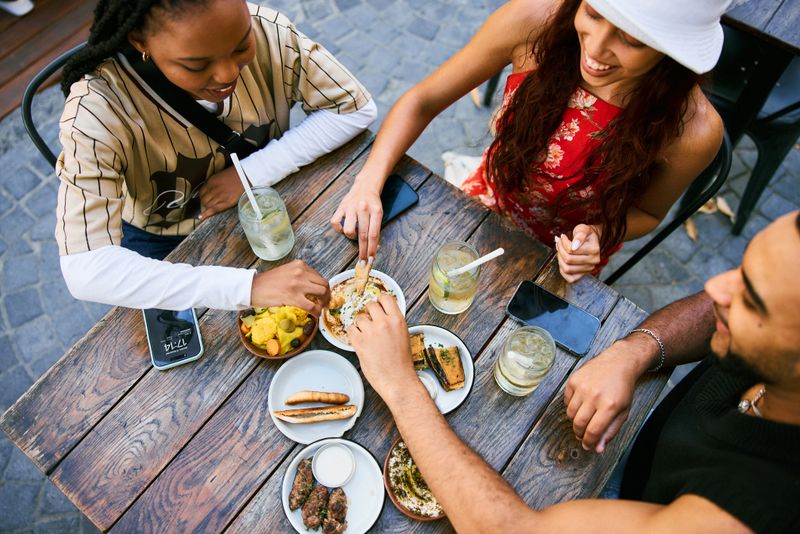 High angle view of young adults sitting around a cafe table, sharing plates and drinks while enjoying connection, laughter, and casual city dining.