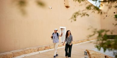 Couple walking and laughing outdoors near a beige wall.
