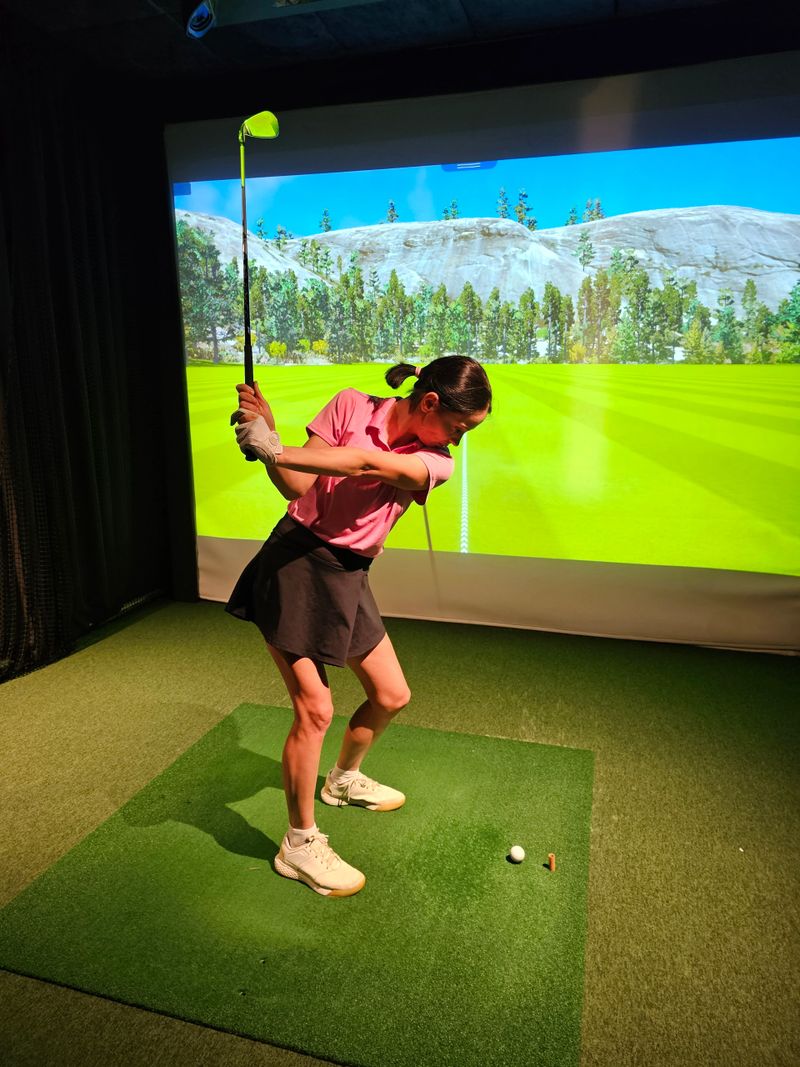Golfer prepares to swing in indoor simulator at sports facility during the afternoon