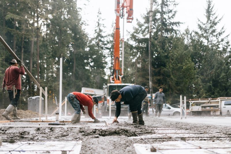A team of hardworking men spreading, leveling, and pouring concrete at a construction site, preparing the slab for a new home build.  A crane pump pours fresh cement from a cement truck.