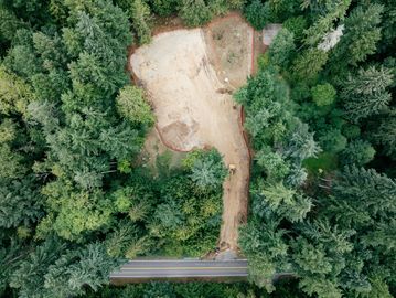 A cleared land patch surrounded by dense forest with a road at the bottom.