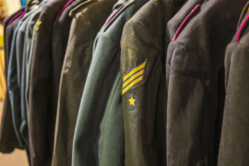 Row of vintage military uniforms hanging on rack in warm light