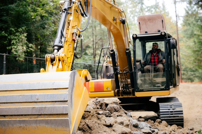 A Caucasian construction worker operates a large excavator to clear the lot on a property to make way for the building of a new home.  Breaking ground.  Shot in the Pacific Northwest.