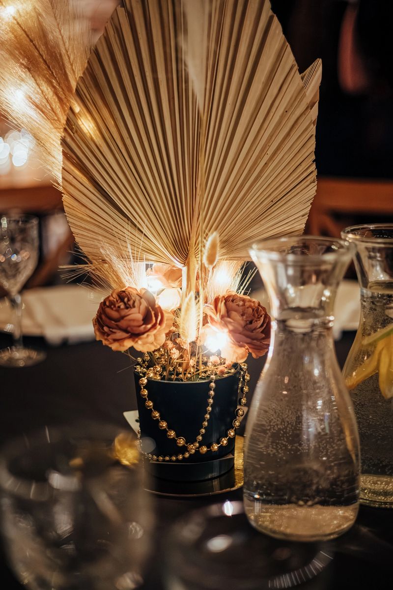 Sophisticated table setting with crystal glassware, white napkins, and a golden dried floral centerpiece with warm lighting. Ideal for upscale events. Contains copy space