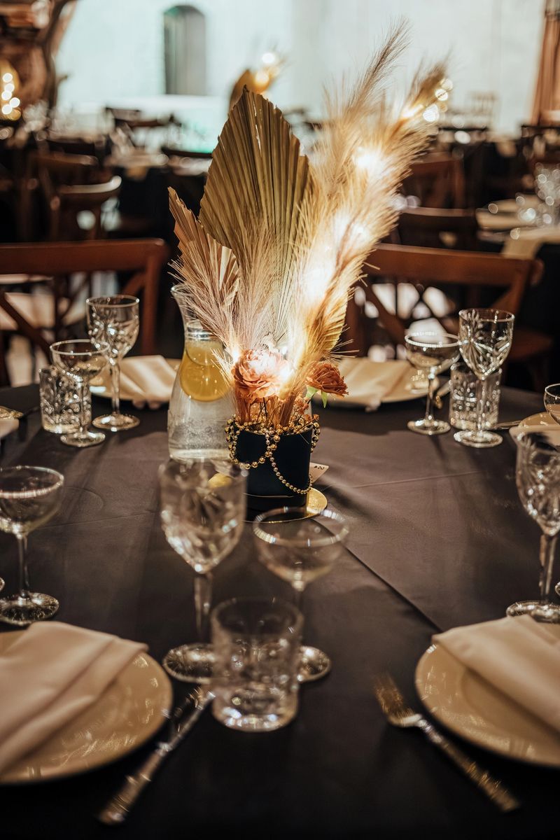 Sophisticated table setting with crystal glassware, white napkins, and a golden dried floral centerpiece with warm lighting. Ideal for upscale events. Contains copy space