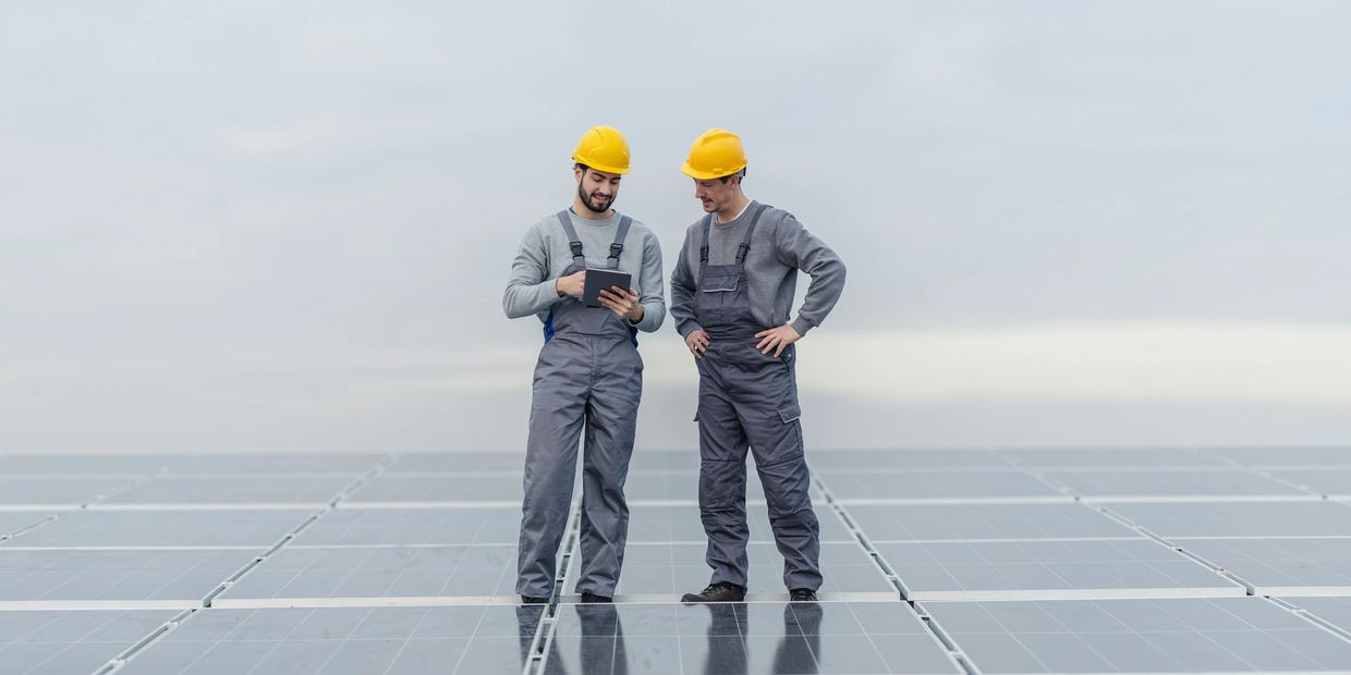 Two workers in helmets inspecting solar panels with a tablet.