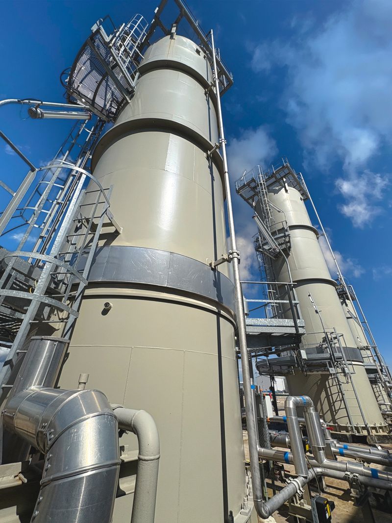 Large industrial processing towers with metal platforms and pipes against a blue sky. Modern chemical or gas plant infrastructure, heavy industry, energy production and technology concept.