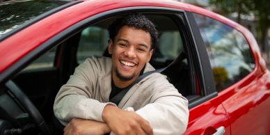 Young man sitting in red car looking out the window smiling