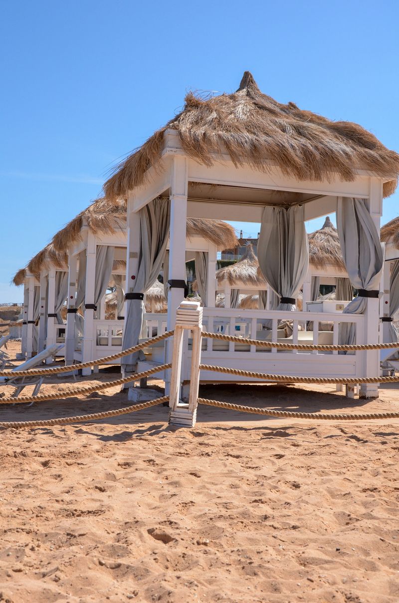 A row of elegant beach cabanas with thatched roofs on a sandy beach, perfect for relaxation and sunbathing.