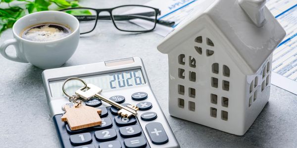 Calculator, house model, keys, glasses, and coffee cup on table.
