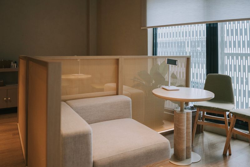 Modern spa lounge interior featuring sofa seating, privacy partition, and a round table by natural window light, conveying comfort, relaxation, wellness, and a calm premium waiting area atmosphere. Kuala Lumpur