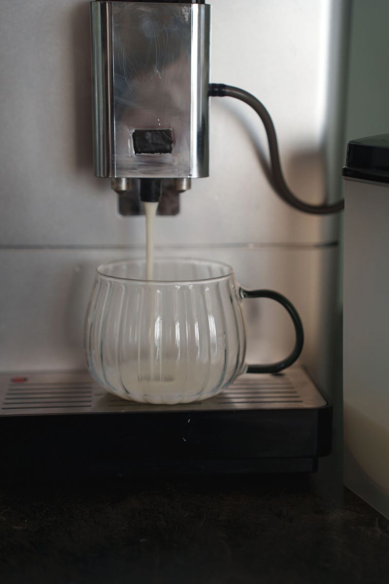 close-up of coffee machine pouring liquid into an elegant ribbed glass mug on a sleek kitchen counter, highlighting modern appliance design and warm lighting ambiance, ritual, elegant, industrial