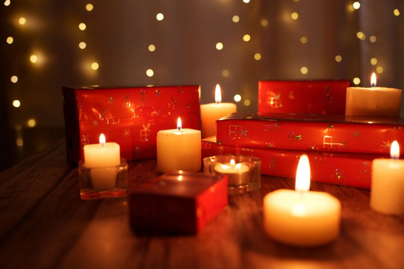 warm and cozy holiday ambiance with flickering candlelight and red gift boxes surrounded by soft, glistening bokeh lights on a rustic wooden table, new, reflection, candlelight, glowing, arrangement