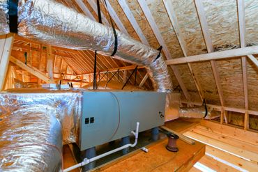 HVAC system installed in an attic with wooden framing and insulation.