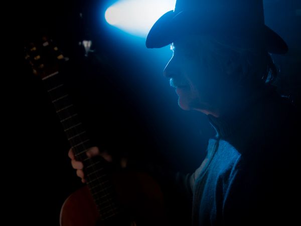 Silhouette of a man wearing a cowboy hat with a guitar in dim blue light.