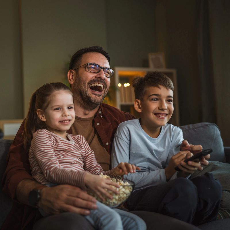 Family enjoying a cozy movie night at home, sharing popcorn and moments of connection and happiness while relaxing together on the couch in the living room