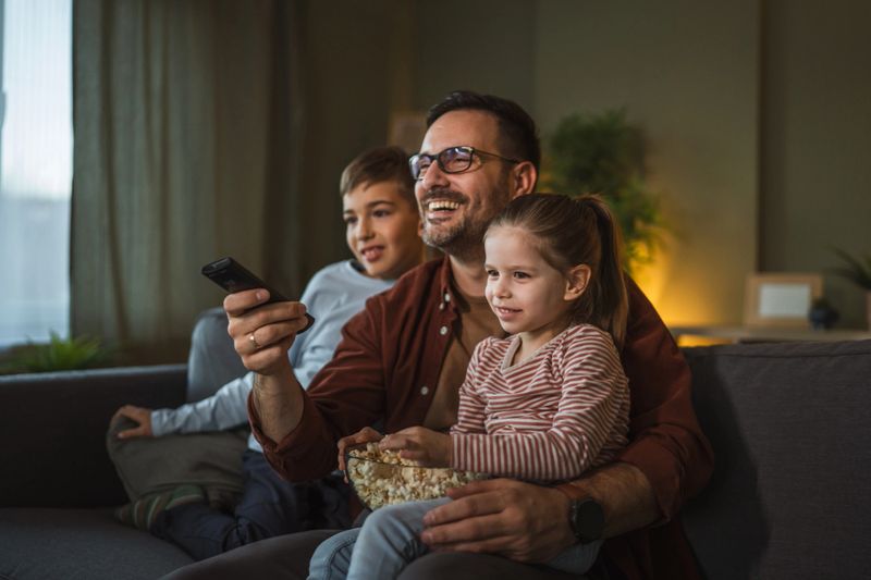 Family enjoying a cozy movie night at home, sharing popcorn and moments of connection and happiness while relaxing together on the couch in the living room