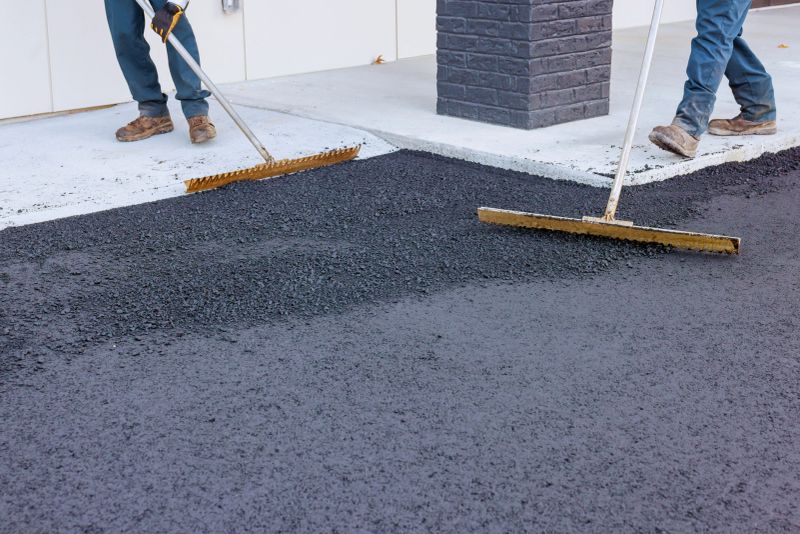 Workers use large rakes to spread freshly laid asphalt at busy construction site