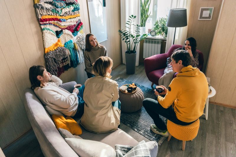 Psychologist leading group therapy session with adult clients in warm counseling office. Concept of psychological support, therapeutic help, trust, communication, mental health care and recovery.