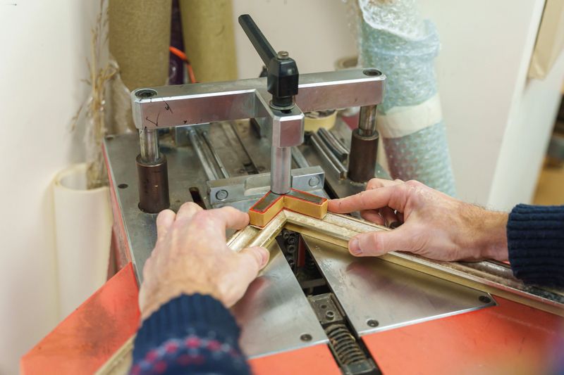 Hands of a craftsman using a professional underpinning machine to join a wooden picture frame. High quality photo