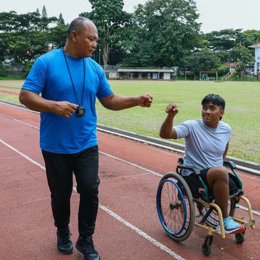 Coach fist-bumps athlete in wheelchair on track.