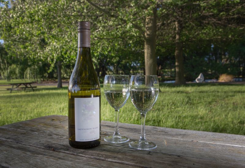 At a winery at Blenheim South Island. Bottle white wine and glasses at wooden table.