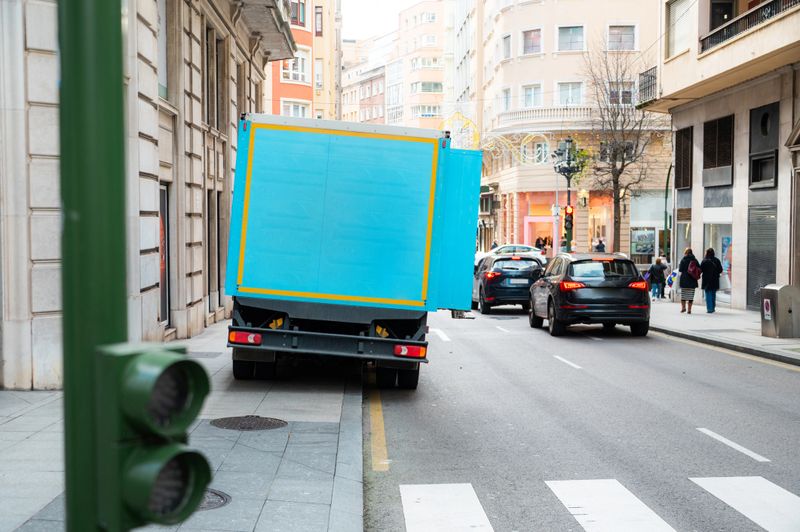 Delivery truck parked with two wheels on the sidewalk in an urban street. Concept of urban logistics, last-mile delivery, traffic, and city infrastructure.