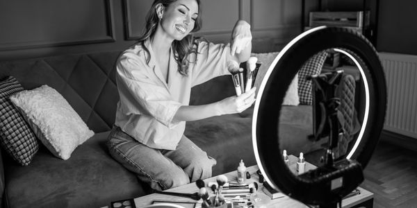 Woman recording beauty tutorial with makeup brushes.