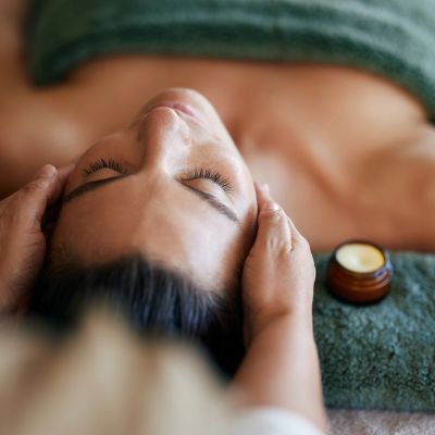 Person receiving a facial massage with cream nearby.