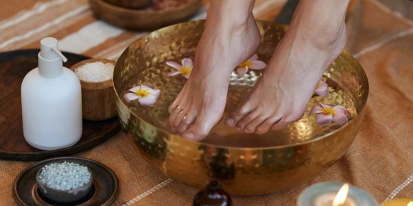 Feet soaking in a brass bowl with flowers for a spa treatment.