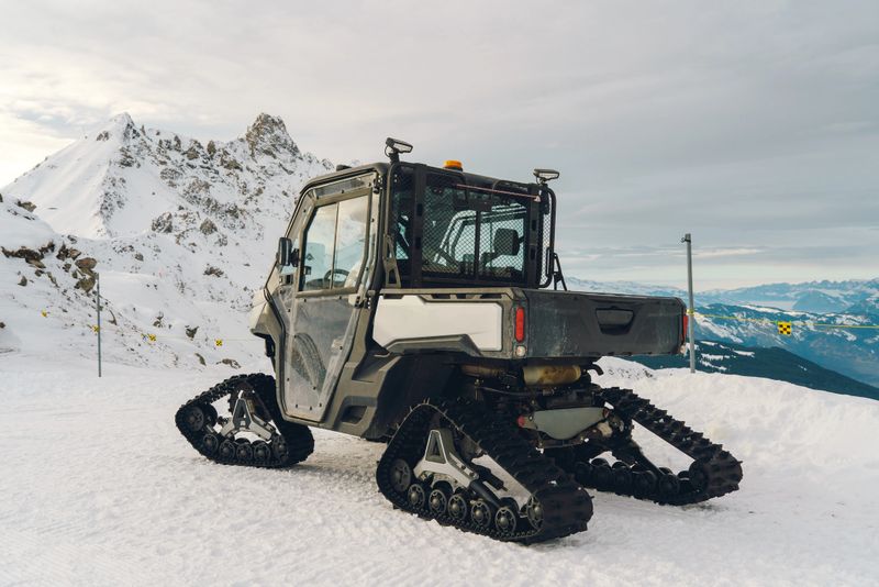 Utility vehicle with tracks resting on fresh snow with mountains in background