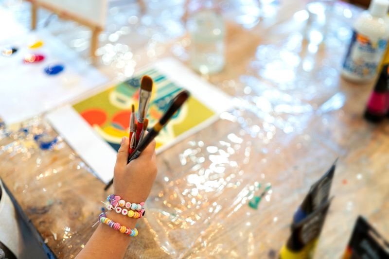Kid holding artist paintbrushes with colorful beads bracelet during art and family painting workshop